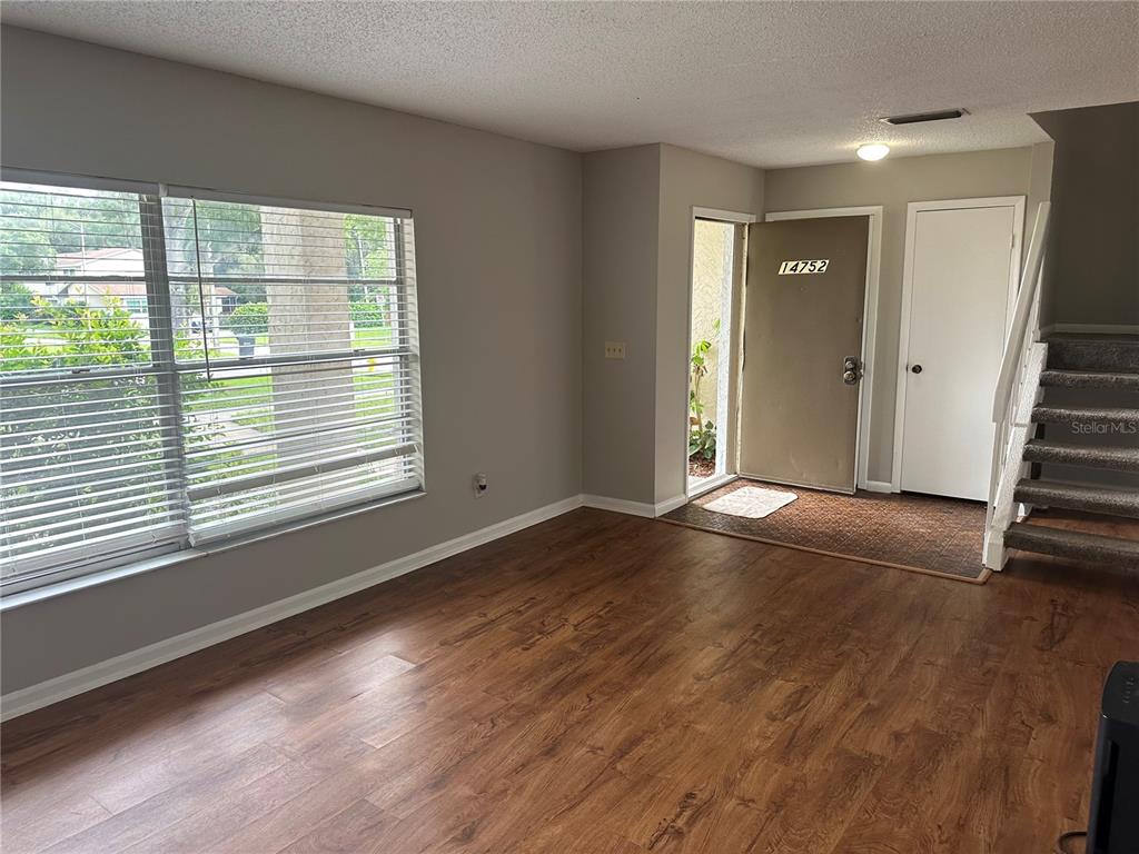 A living room features wood-look flooring, a large window with blinds, and an entryway door — 14752 MORNING DRIVE, LUTZ, FL