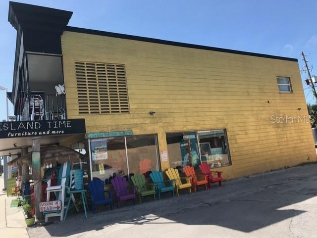 A yellow two-story commercial building with a row of colorful Adirondack chairs in front — 431 75TH AVENUE, ST PETE BEACH, FL