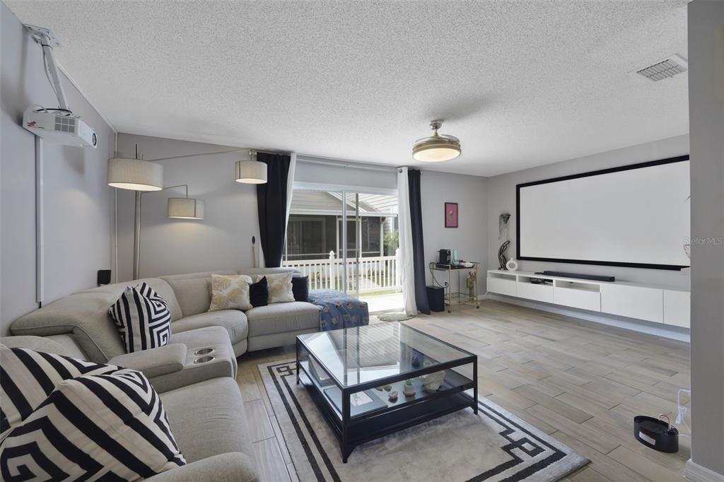 A living room features a projector, a large screen, a sectional sofa, and glass coffee table — 942 SYKES COURT UNIT 101, ORLANDO, FL