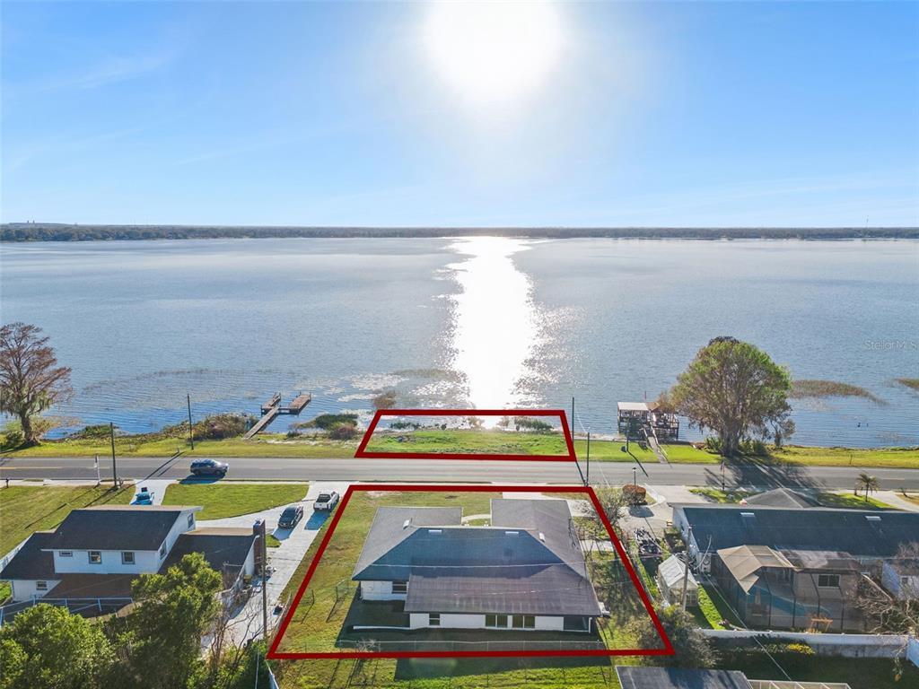 An aerial view shows three houses across a road from a lakefront grassy lot — 1106 LAKE ARIANA BOULEVARD, AUBURNDALE, FL