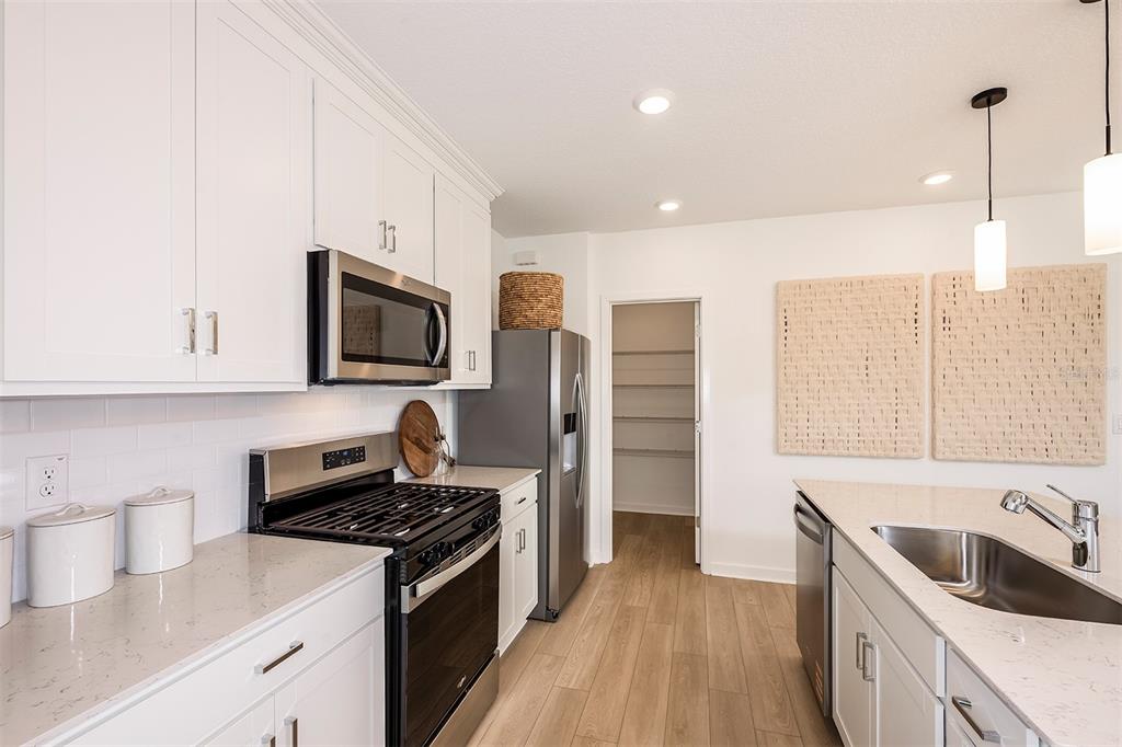 A modern kitchen features white cabinets, stainless steel appliances, quartz countertops, and a walk-in pantry — 9736 CRESCENT MOON DRIVE, RIVERVIEW, FL