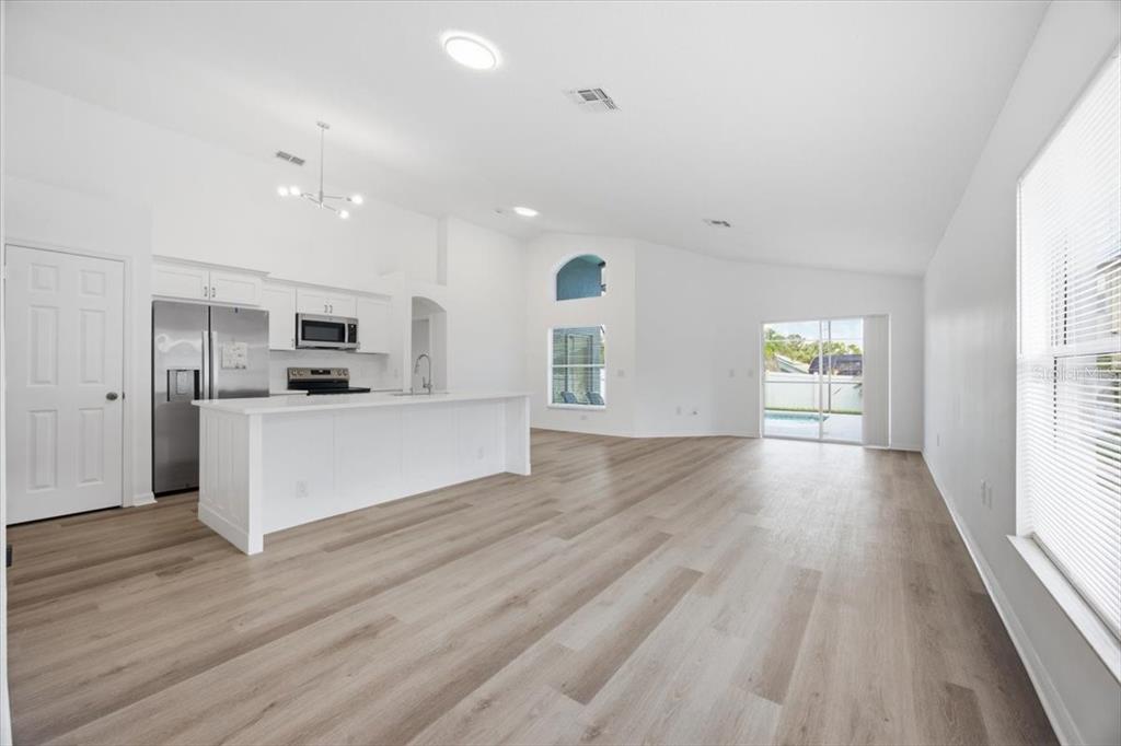 A bright, open-concept kitchen and living area features white cabinetry, a center island, and wood-look flooring — 2712 KOKOMO LOOP, HAINES CITY, FL