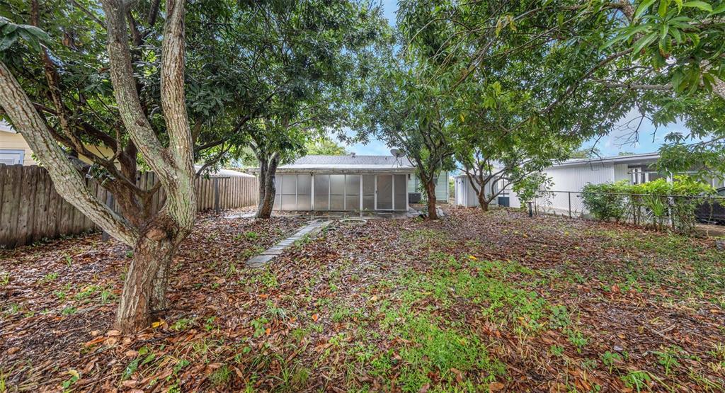 A backyard with mature trees, a screened-in patio, and a wooden fence — 5621 11TH AVENUE N, ST PETERSBURG, FL