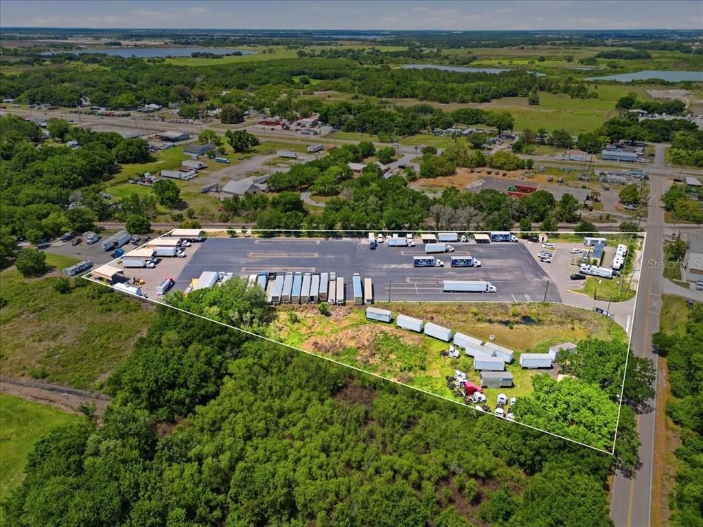 An aerial view shows a paved lot with parked semi-trailers surrounded by trees and roads — 100 S AIRPORT ROAD, LAKE WALES, FL