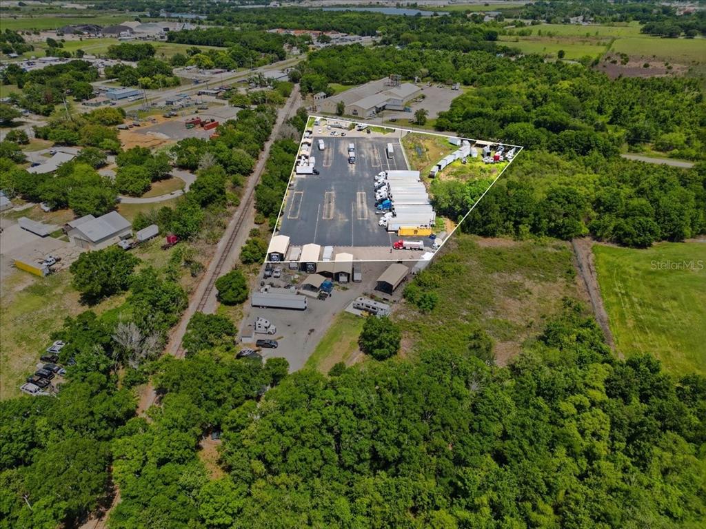 An aerial view shows a commercial trucking lot with parked trailers surrounded by dense trees — 100 S AIRPORT ROAD, LAKE WALES, FL