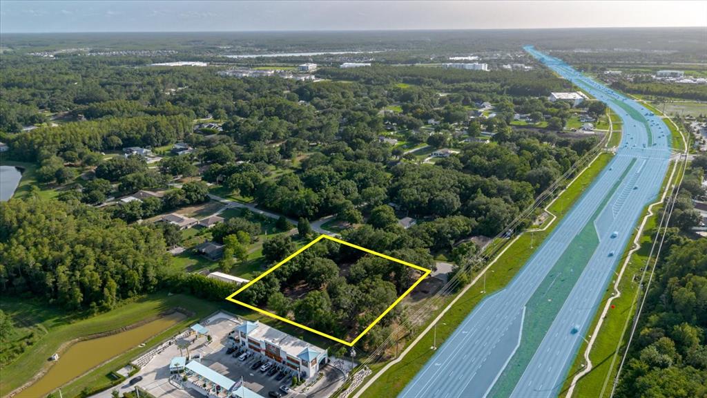 An aerial view shows a vacant, tree-covered lot outlined in yellow next to a highway — 17380 RIVERSTONE DRIVE, LUTZ, FL