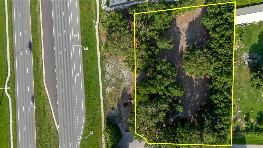 An aerial view shows a rectangular, tree-lined vacant lot adjacent to a multi-lane highway — 17380 RIVERSTONE DRIVE, LUTZ, FL