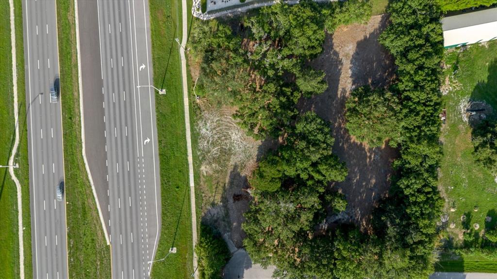 An aerial view shows a vacant, tree-lined lot adjacent to a multi-lane highway — 17380 RIVERSTONE DRIVE, LUTZ, FL