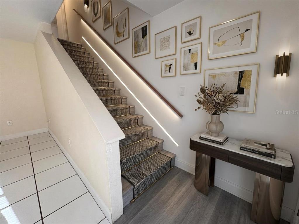 A staircase with a runner and integrated lighting sits beside a console table and gallery wall — 4033 HENLEY ROAD UNIT 1707, ORLANDO, FL