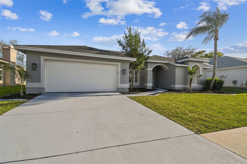 A single-story suburban house features a two-car garage, gray stucco exterior, and arched windows — 8818 POE DRIVE, HUDSON, FL