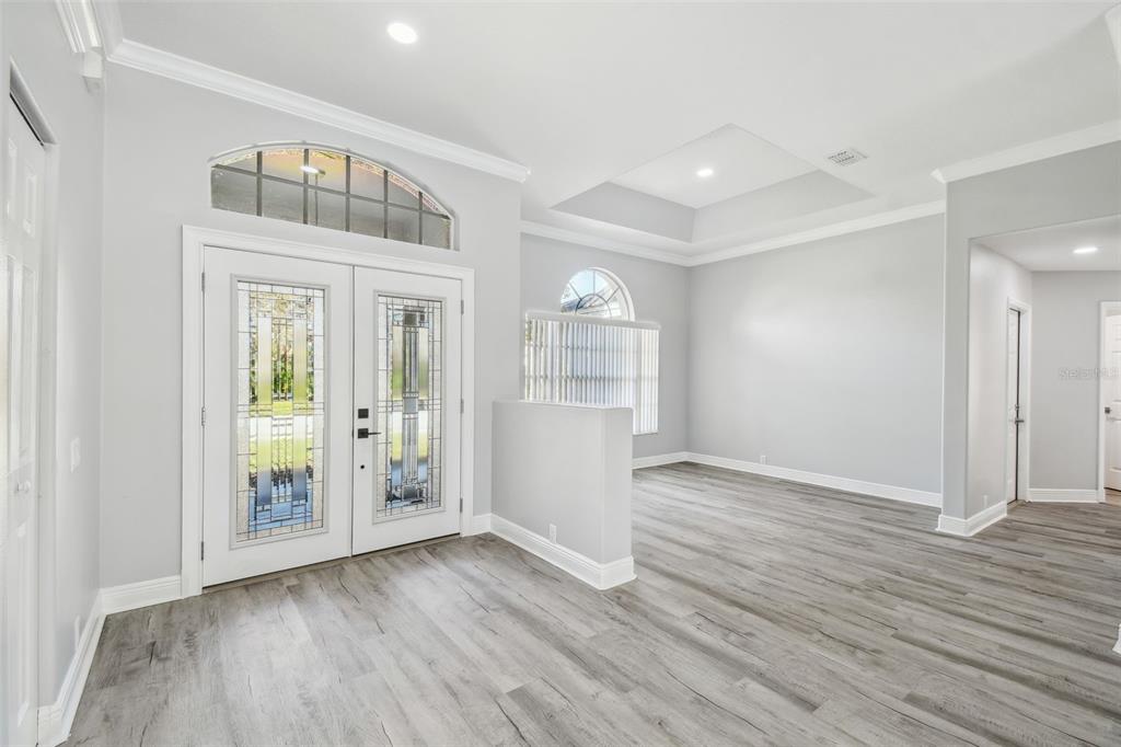 An entryway with gray wood-look flooring, double glass-paneled doors, and a tray ceiling — 8818 POE DRIVE, HUDSON, FL