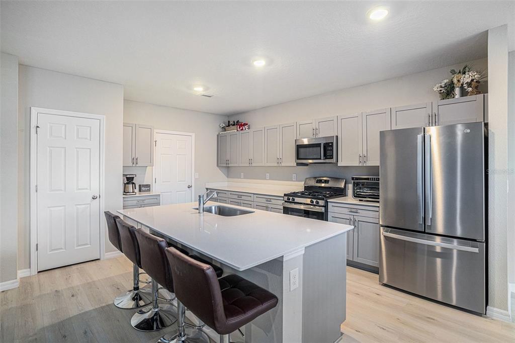 A modern kitchen features a central island with bar seating, gray cabinetry, and stainless appliances — 12940 HAWKSTONE TRAIL BOULEVARD, LITHIA, FL