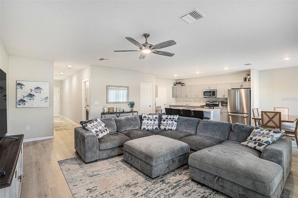 A spacious open-concept living room features a large gray sectional sofa and a modern kitchen — 12940 HAWKSTONE TRAIL BOULEVARD, LITHIA, FL