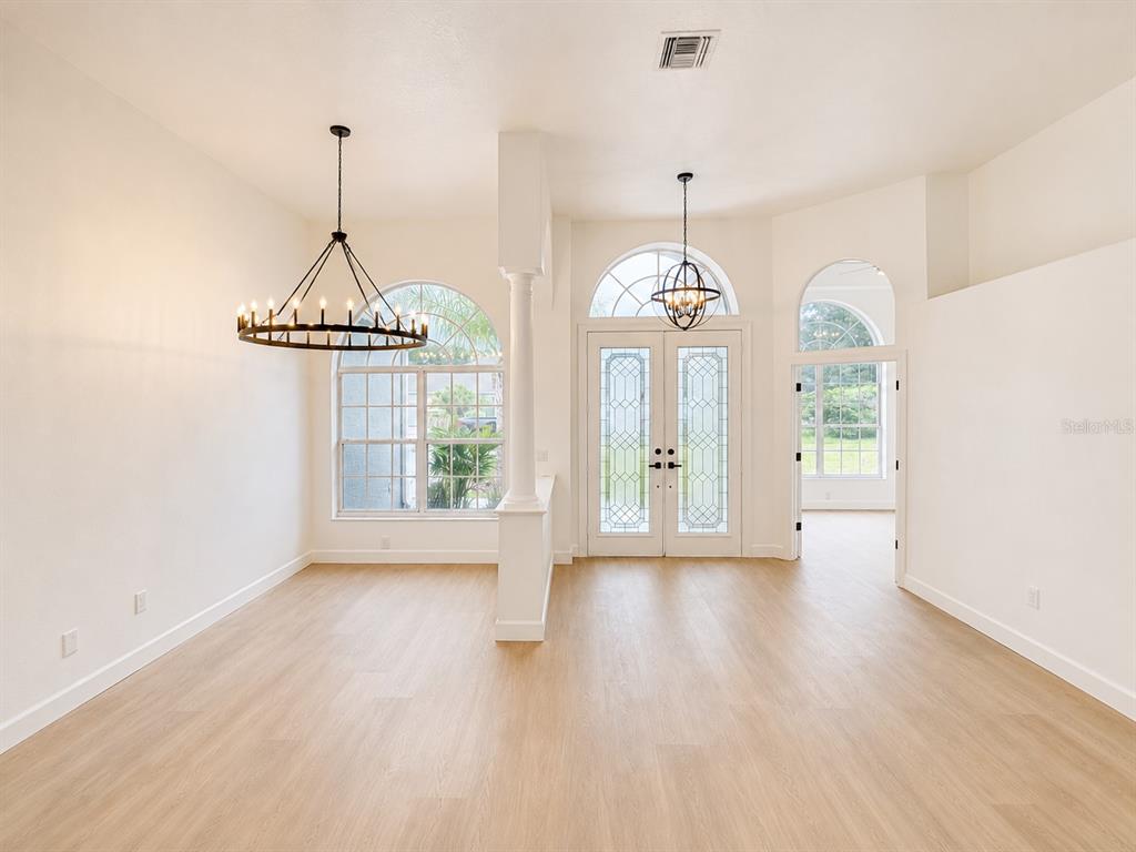 A bright dining area features light wood flooring, two chandeliers, and arched windows and doors — 2532 BELLWOOD DRIVE, BRANDON, FL