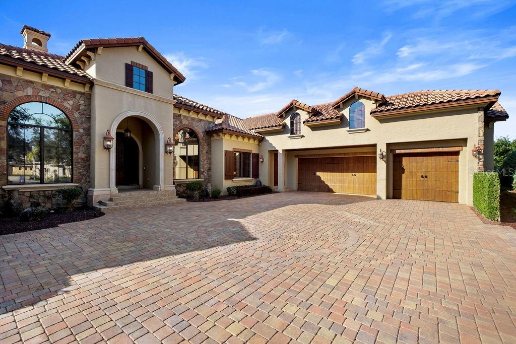A large Mediterranean-style house features a stone facade, arched entryway, and a paved driveway — 6130 GROSVENOR SHORE DRIVE, WINDERMERE, FL