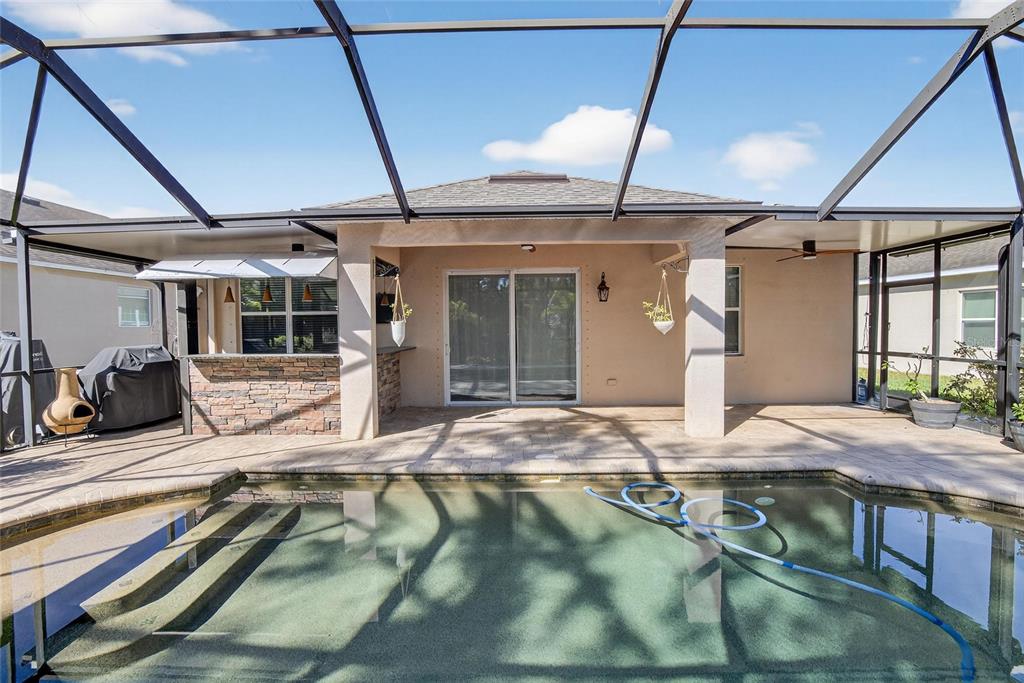 A covered patio with a stone bar overlooks a swimming pool inside a screened enclosure — 9023 41ST STREET E, PARRISH, FL