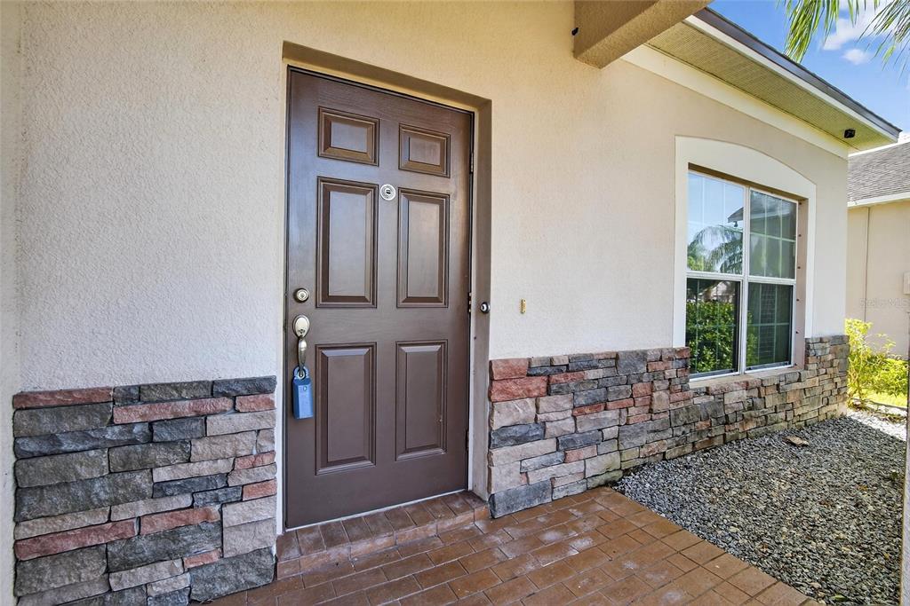 A brown front door with a lockbox sits beside a stone-accented wall and window — 9023 41ST STREET E, PARRISH, FL