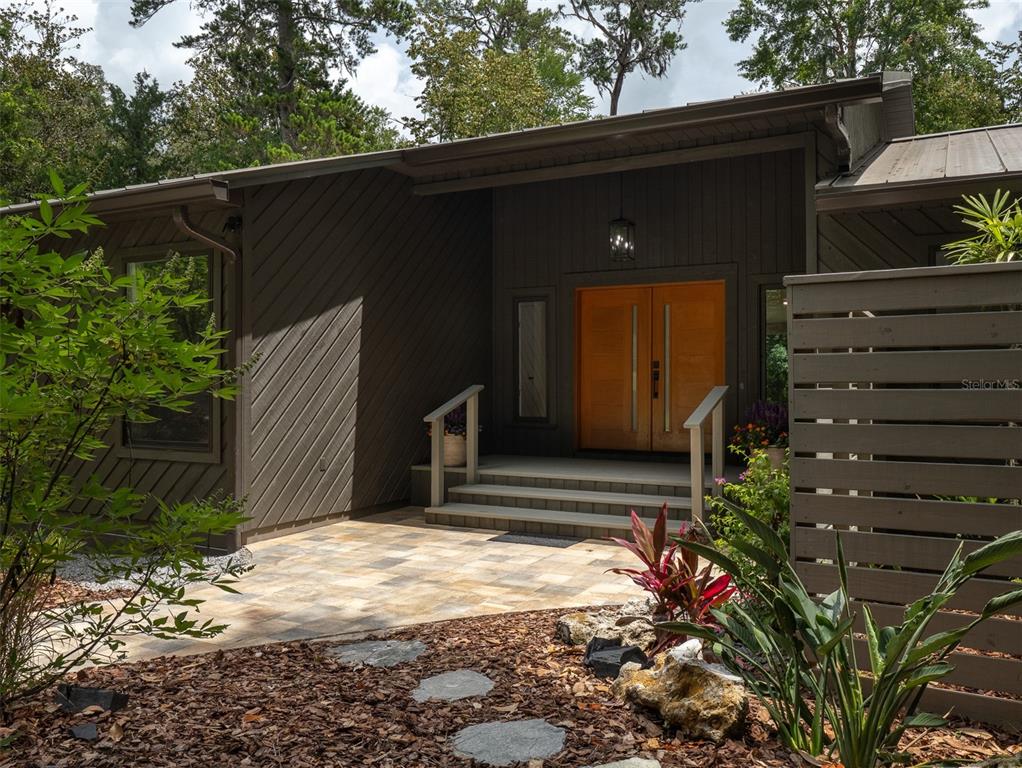 A modern house exterior features a metal roof, diagonal wood siding, and double wooden doors — 3104 NW 21ST AVENUE, GAINESVILLE, FL