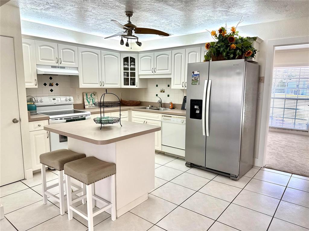 A kitchen features white cabinets, a central island with two stools, and stainless steel appliances — 3715 SHARONDALE DRIVE, SARASOTA, FL
