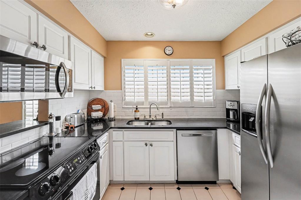 A kitchen features white cabinets, black countertops, stainless steel appliances, and white subway tile backsplash — 3053 S CONCORDIA AVENUE UNIT A, TAMPA, FL