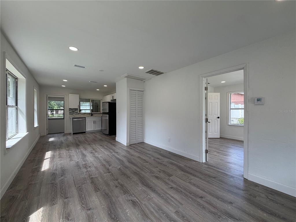 A bright living area with wood-look flooring leads to a kitchen and an adjacent room — 234 N ADAMS STREET, DAYTONA BEACH, FL