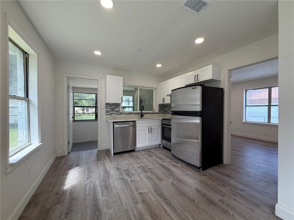 A kitchen features white cabinets, stainless steel appliances, and wood-look flooring — 234 N ADAMS STREET, DAYTONA BEACH, FL