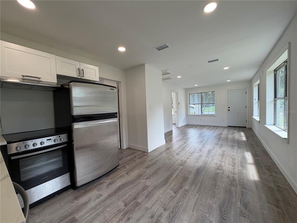 A kitchen with stainless steel appliances and white cabinets opens into a living area — 234 N ADAMS STREET, DAYTONA BEACH, FL