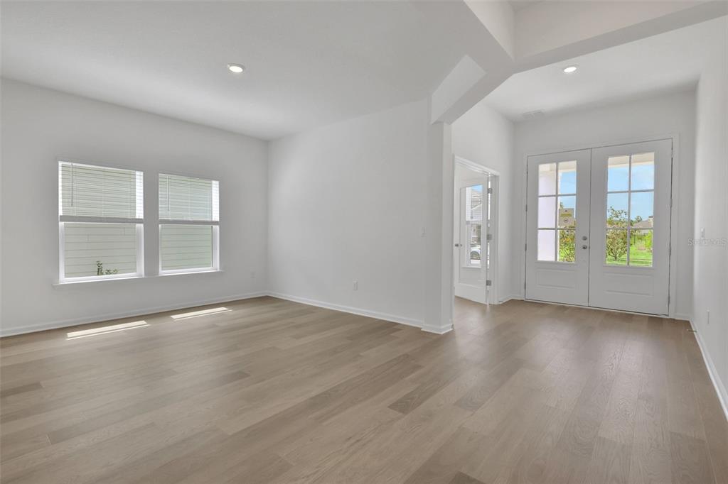 An empty room with light wood flooring, white walls, large windows, and double glass doors — 3217 WILLOWLEAF LANE, GREEN COVE SPRINGS, FL