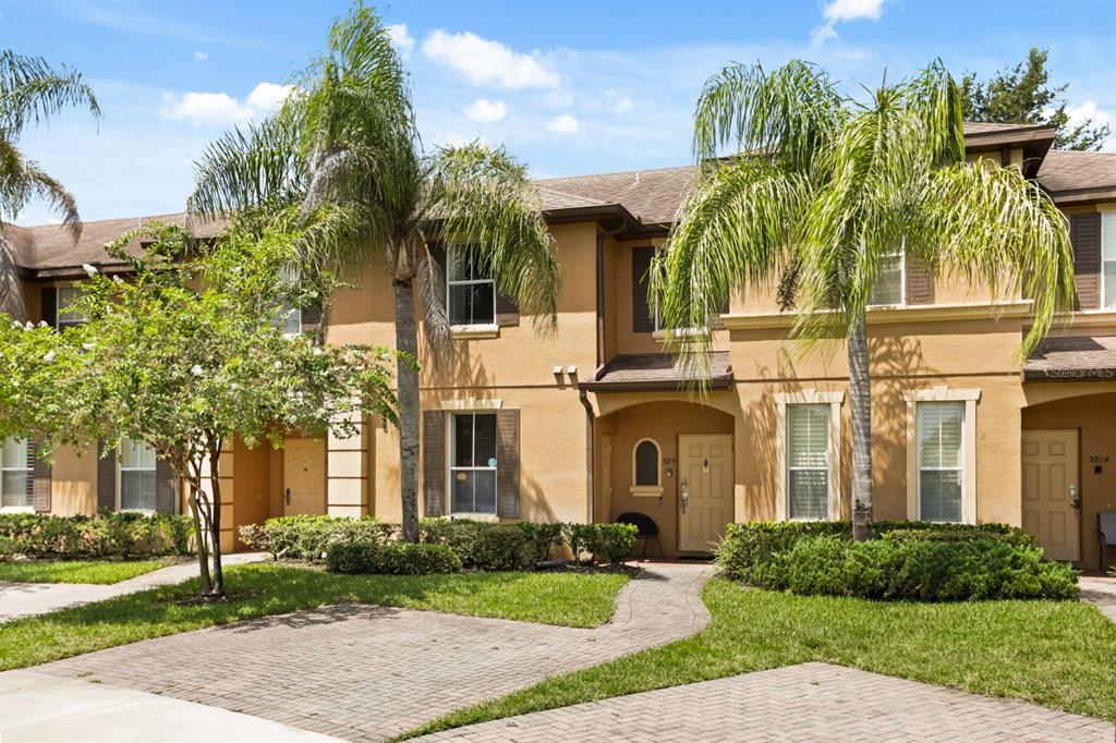 A two-story tan stucco townhouse with palm trees and a brick paver driveway — 3214 CALABRIA AVENUE UNIT 3214, DAVENPORT, FL