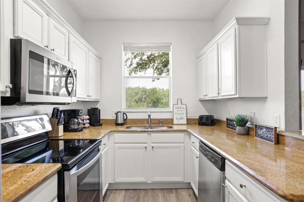 A galley kitchen features white cabinets, granite countertops, stainless steel appliances, and a window view — 3214 CALABRIA AVENUE UNIT 3214, DAVENPORT, FL