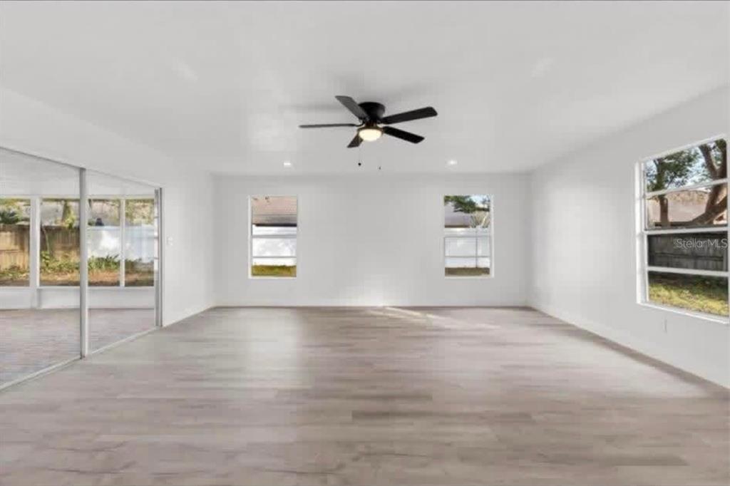 An empty room with light wood-look flooring, white walls, a ceiling fan, and large windows — 14915 GENTILLY PLACE, TAMPA, FL