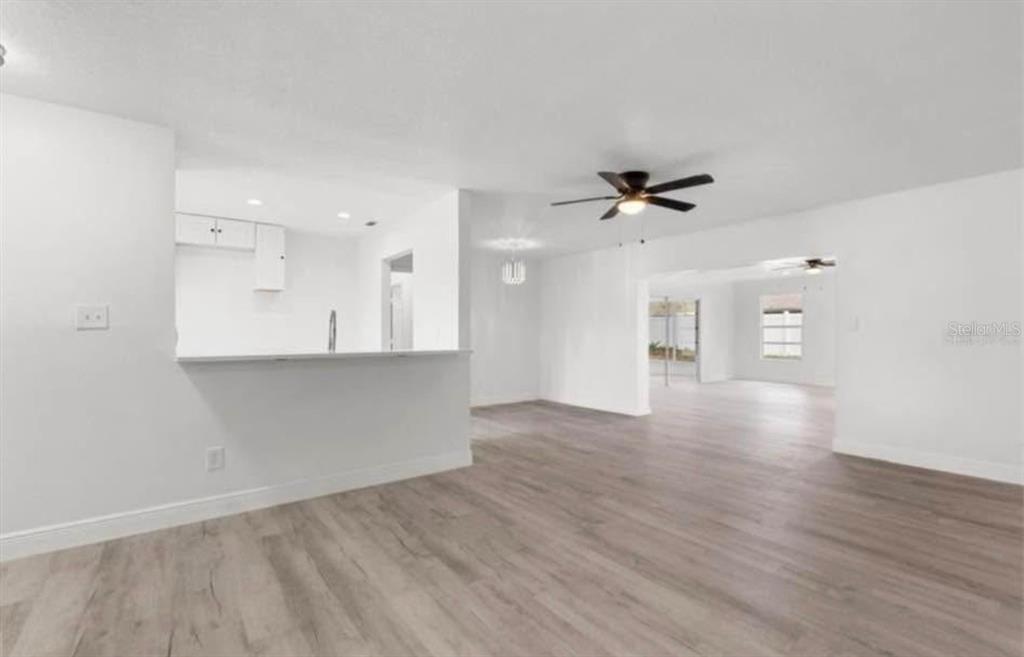 An open-concept living area features light wood-look flooring, white walls, and a kitchen breakfast bar — 14915 GENTILLY PLACE, TAMPA, FL
