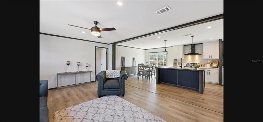 An open-concept living room and kitchen featuring light wood flooring and a dark kitchen island — 1636 MISTLETOE STREET, BUNNELL, FL