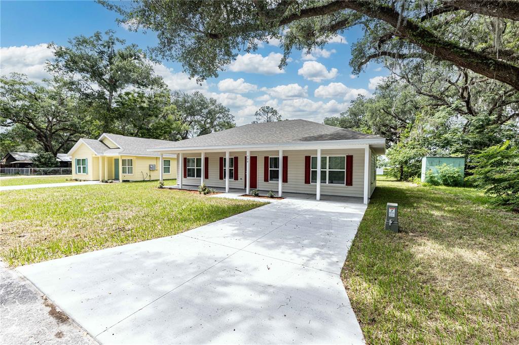 A beige single-story house with a white front porch and red shutters sits on a lawn — 306 E GEORGIA AVENUE, BUSHNELL, FL