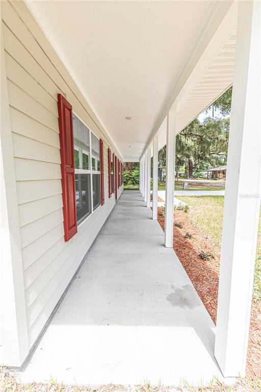 A long, covered concrete porch runs along the side of a house with beige siding — 306 E GEORGIA AVENUE, BUSHNELL, FL
