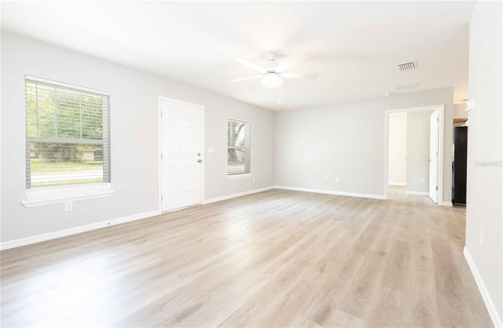 A bright living room features light wood-look flooring, white walls, and a ceiling fan — 306 E GEORGIA AVENUE, BUSHNELL, FL