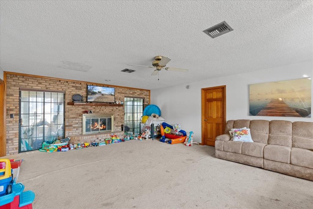 A living room features a brick fireplace, beige carpeting, a ceiling fan, and a sofa — 910 WHITEWOOD DRIVE, DELTONA, FL