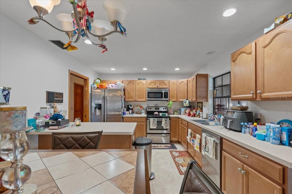 A kitchen features light wood cabinets, stainless steel appliances, and a tiled dining table — 910 WHITEWOOD DRIVE, DELTONA, FL