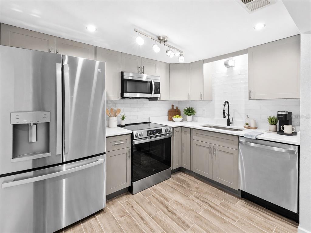 A kitchen features stainless steel appliances, light gray cabinets, white countertops, and wood-look tile flooring — 505 PLAZA SEVILLE COURT UNIT 9, TREASURE ISLAND, FL