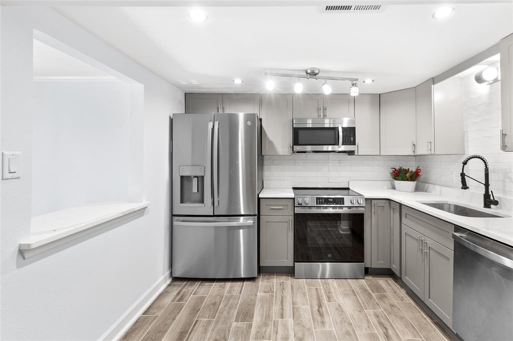 A kitchen features gray cabinets, stainless steel appliances, white subway tile backsplash, and wood-look flooring — 505 PLAZA SEVILLE COURT UNIT 9, TREASURE ISLAND, FL