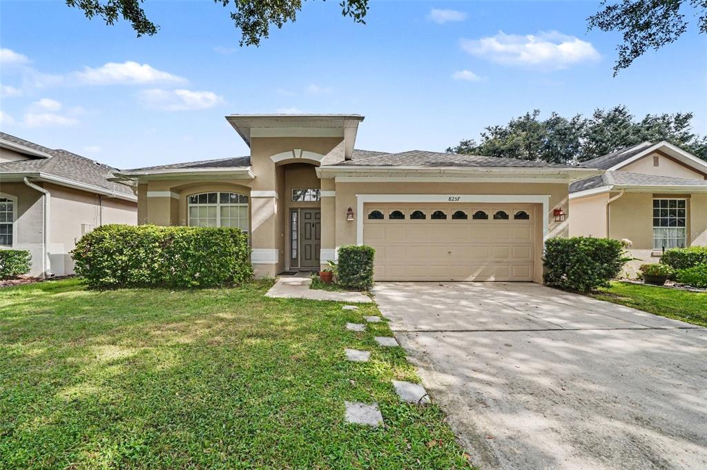 A single-story suburban house with a tan stucco exterior, a two-car garage, and a lawn — 8257 BAYWOOD VISTA DRIVE, ORLANDO, FL