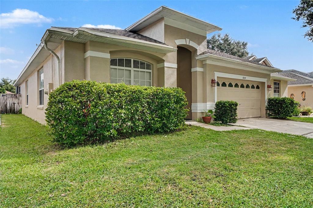 A single-story tan house with a two-car garage and a large hedge in the front — 8257 BAYWOOD VISTA DRIVE, ORLANDO, FL