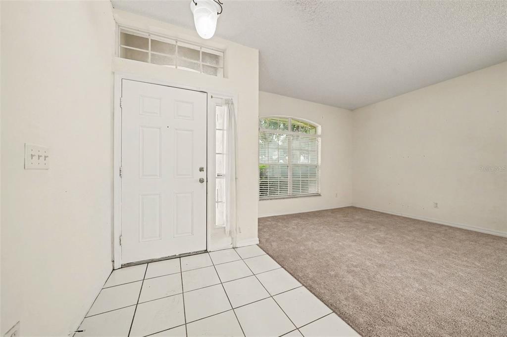 An entryway with white tile flooring leads into a carpeted living room with a front door — 8257 BAYWOOD VISTA DRIVE, ORLANDO, FL