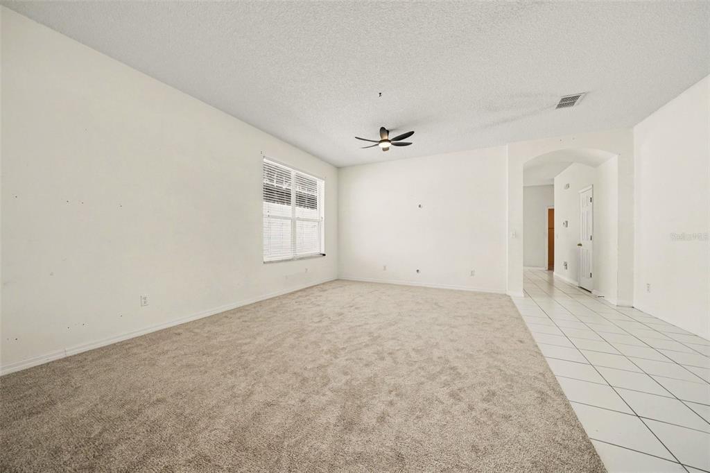 An empty living room features beige carpeting, white walls, a ceiling fan, and tiled flooring — 8257 BAYWOOD VISTA DRIVE, ORLANDO, FL