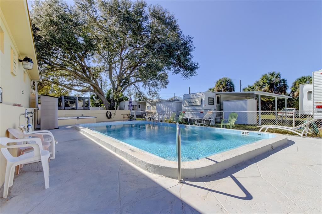 A rectangular swimming pool sits on a concrete patio next to a house and trailers — 4677 66TH LANE N UNIT 1, ST PETERSBURG, FL