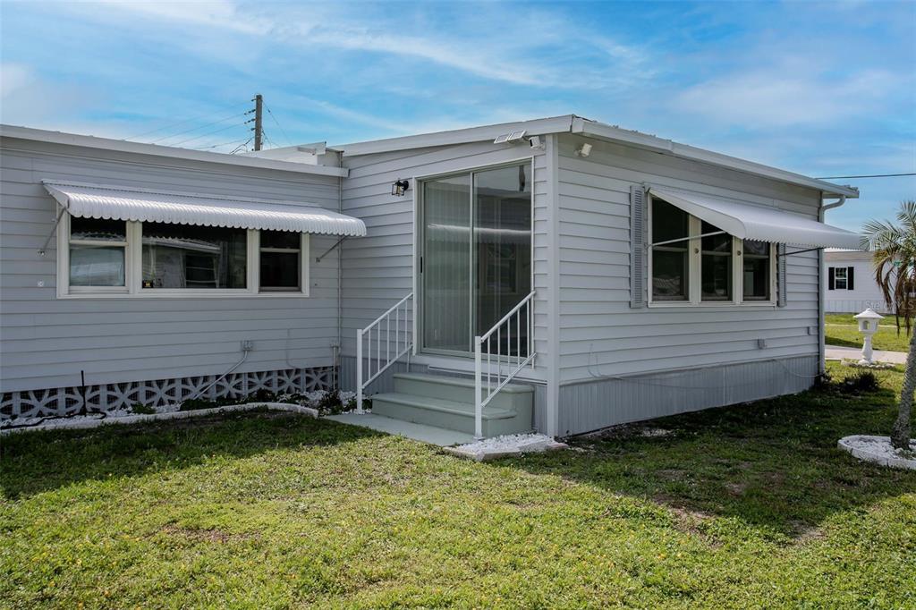 A light gray mobile home exterior features white window awnings, a sliding glass door, and stairs — 5105 8TH STREET W, BRADENTON, FL