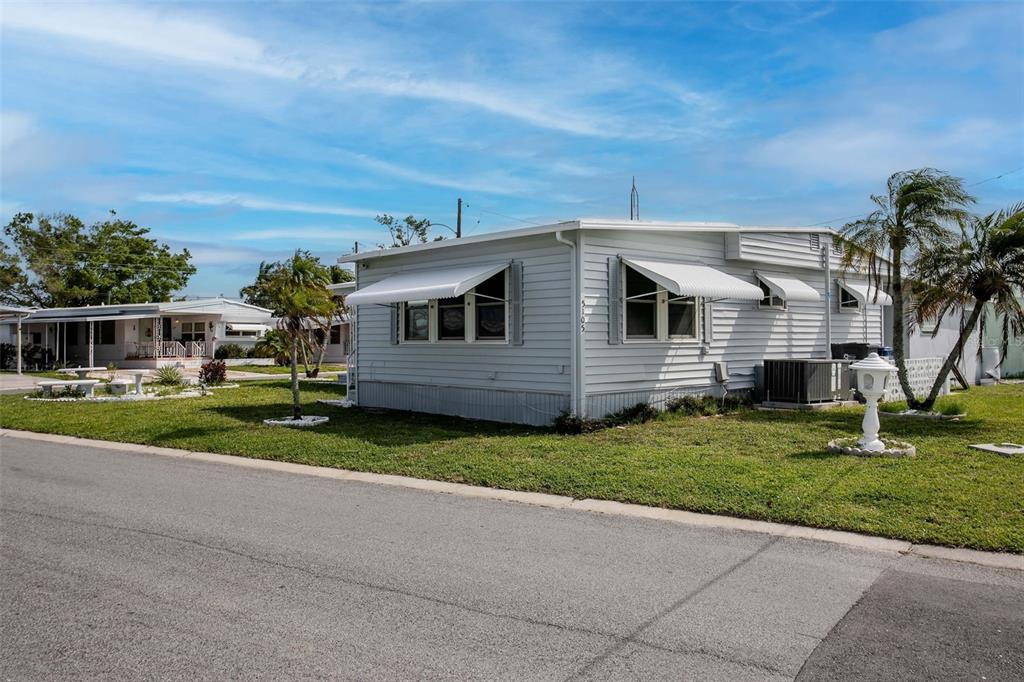 A light-colored mobile home with white awnings sits on a grassy lot near a road — 5105 8TH STREET W, BRADENTON, FL