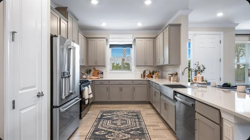 A kitchen features gray cabinets, stainless steel appliances, a farmhouse sink, and light-colored countertops — 4305 ROSATTI ROAD, WESLEY CHAPEL, FL