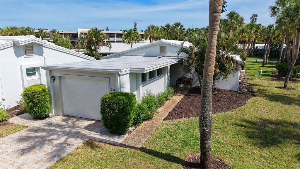 A white single-story house features a garage, a covered entryway, and surrounding palm trees — 206 HOURGLASS WAY UNIT V10, SARASOTA, FL