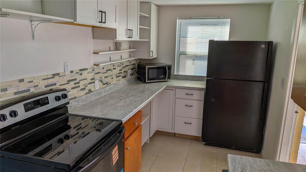 A kitchen features white cabinets, a black refrigerator, a black stove, and a tiled backsplash — 11301 110TH TERRACE, LARGO, FL